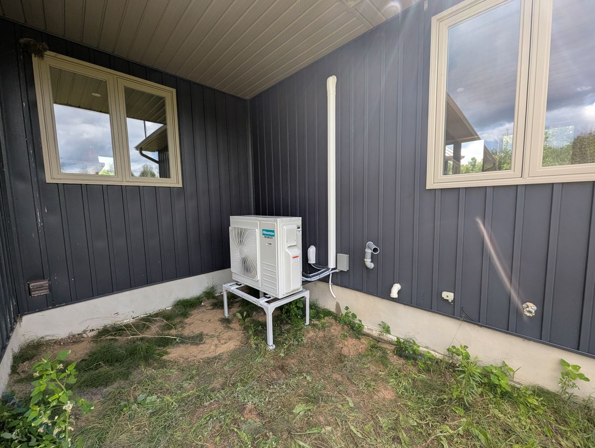 Hisense heat pump installed on a raised stand beside dark siding